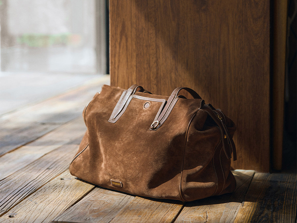 Brown suede tote bag on a wooden floor near a window