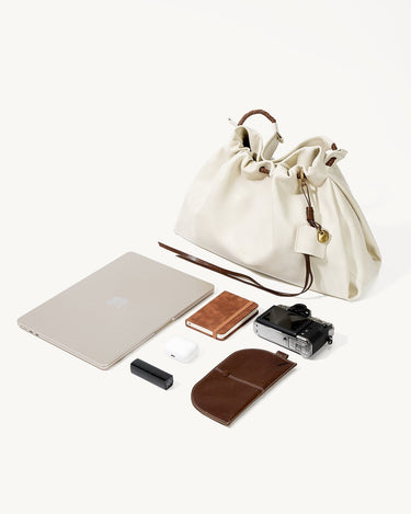 Light ivory medium gather bag with laptop, camera, earbuds, notebook, and leather case.