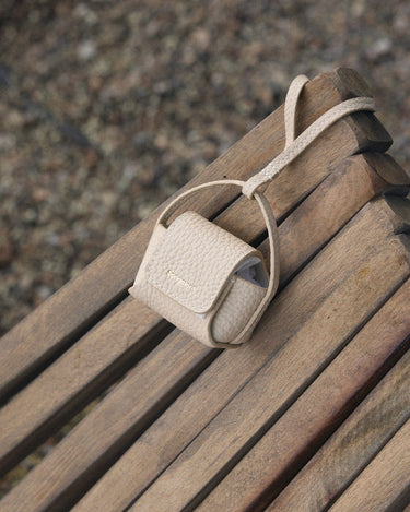 Songmont full-grain leather AirPods case in beige with magnetic closure and embossed logo.