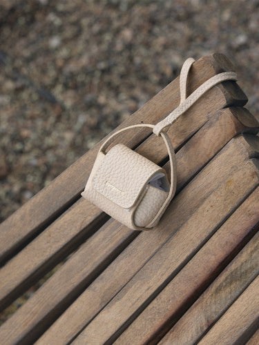 Songmont full-grain leather AirPods case in beige with magnetic closure and embossed logo.