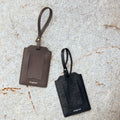 Songmont leather luggage tags in dark brown and black on a textured stone surface
