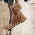 Songmont Puppy Charm accessory in tan and brown leather with white stitching on a beige handbag.