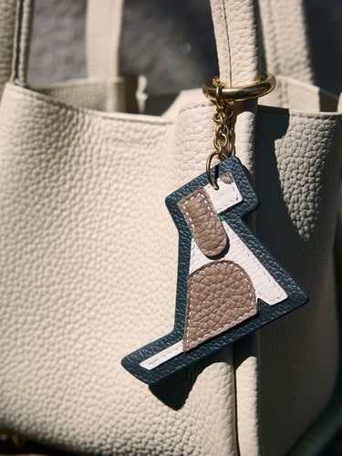 Songmont Puppy Charm accessory with navy blue trim and brown, white accents hanging from a cream leather bag.