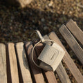 Beige textured full-grain leather Songmont AirPods case with magnetic closure on a wooden bench.