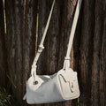 Mini Yore Camera Bag in Cloud color, made of vegetable-tanned leather, hanging on a wooden fence.