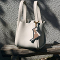 Cream pebble-grain leather handbag with a playful dog-shaped charm dangling from the handle.