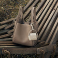 Songmont taupe full-grain leather tote bag with cream AirPods case attached, featuring magnetic closure and 'Songmont' text.