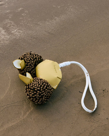 Yellow leather crab charm with textured brown body and white strap on sand
