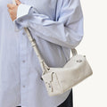 Model wears a light blue pinstripe shirt and a cream-colored Mini Yore Camera Bag from Songmont.