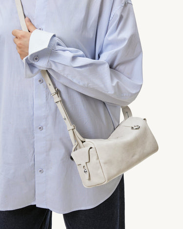 Model wears a light blue pinstripe shirt and a cream-colored Mini Yore Camera Bag from Songmont.