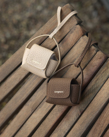 Songmont full-grain leather AirPods cases in beige and brown with flap closure and embossed logo