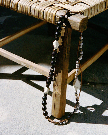 Large Carefree Thread Charm Sandal: dark beads, leather diamonds, seed beads on wooden stool.