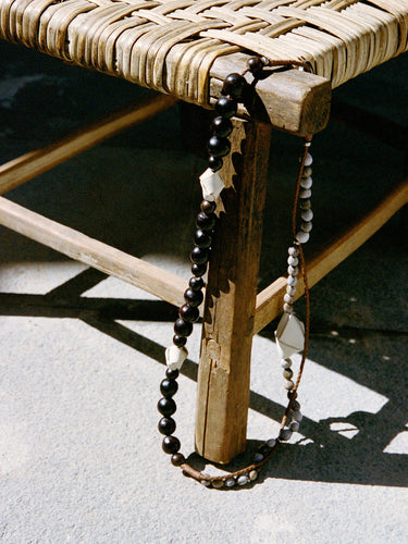 Large Carefree Thread Charm Sandal: dark beads, leather diamonds, seed beads on wooden stool.