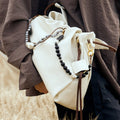 Cream leather Carefree Thread Charm bag with wood & grey beads, braided handles. Model in brown.