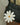 White leather daisy charm with yellow center, attached to a black handbag strap.