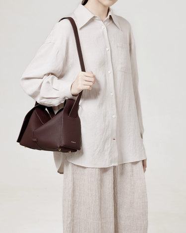 Burgundy leather Drippy Roof Bag with gold hardware, worn by a model in a light-colored linen outfit.