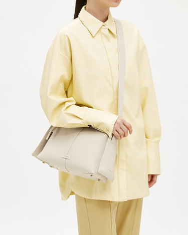 White full-grain leather Drippy Roof Bag with adjustable strap worn by a model in a yellow outfit.