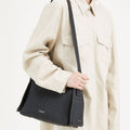 Black full-grain leather Drippy Roof Bag with white stitching, worn by a person in a cream jacket.