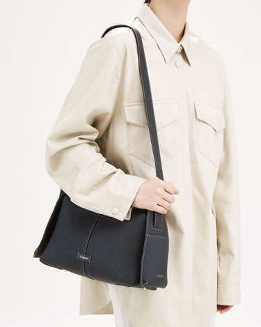 Black full-grain leather Drippy Roof Bag with white stitching, worn by a person in a cream jacket.