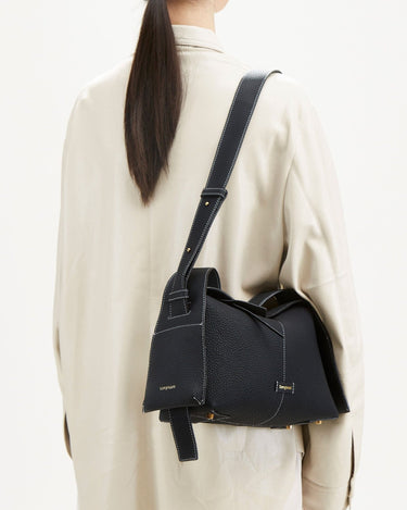 Black full-grain leather Drippy Roof Bag with white stitching and gold hardware, worn by a model.