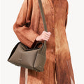 Taupe textured leather Drippy Roof Bag with adjustable strap, held by a person in a brown garment.