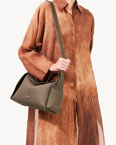 Taupe textured leather Drippy Roof Bag with adjustable strap, held by a person in a brown garment.