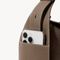 Drippy Roof Bag in taupe pebble leather with a smartphone in an exterior pocket.