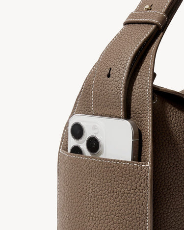 Drippy Roof Bag in taupe pebble leather with a smartphone in an exterior pocket.