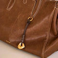 Brown leather Faith Stone Charm with gold hardware, knot detail, and Songmont logo.