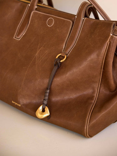Brown leather Faith Stone Charm with gold hardware, knot detail, and Songmont logo.
