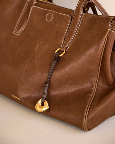 Faith Stone Charm bag in Sandal color, vegetable-tanned leather with white stitching and gold hardware.