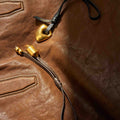Faith Stone Charm in Sandal color with gold-toned hardware and leather strap on a brown leather surface.