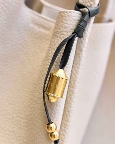 Faith Stone charm detail with brass prayer wheel, engraved patterns, and gold beads on leather strap.