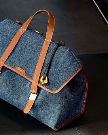 Denim Songmont bag with tan leather trim and straps, featuring a gold buckle.