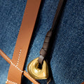 Faith Stone charm with brass finish, on dark brown leather strap, against denim background.