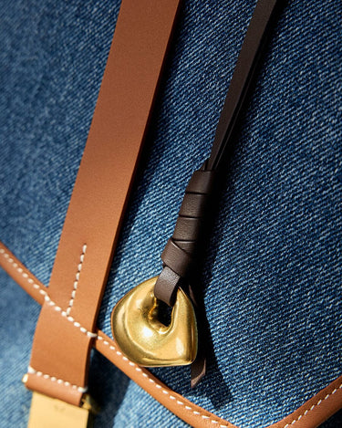 Faith Stone charm with brass finish, on dark brown leather strap, against denim background.