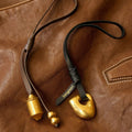 Faith Stone Charm and Prayer Wheel Charm set in Sandal color, made of gold-tone metal and leather.