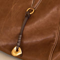 Faith Stone Charm detail on a brown leather bag, featuring a gold-tone charm and a dark brown leather strap.