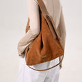 Caramel colored large suede tote bag worn by a model on the shoulder, featuring leather straps and a subtle brand logo.