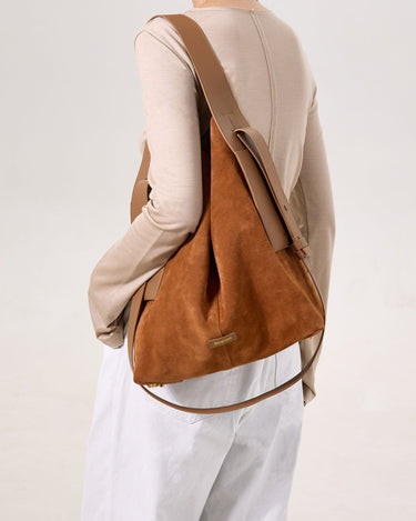 Caramel colored large suede tote bag worn by a model on the shoulder, featuring leather straps and a subtle brand logo.