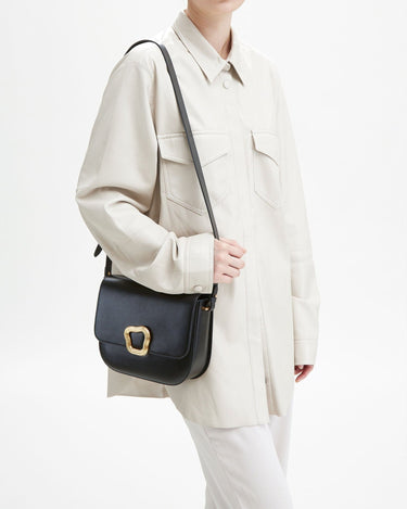 Woman wearing a cream jacket and pants, carrying a black leather Large Reset Tofu Bag with a gold buckle.