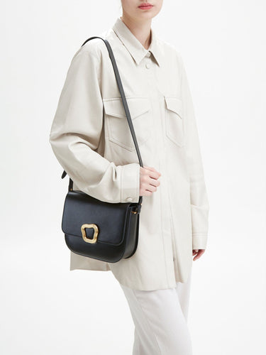 Woman wearing a cream jacket and pants, carrying a black leather Large Reset Tofu Bag with a gold buckle.