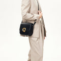Woman wearing a beige suit carries a black calf leather Reset Tofu Bag with a gold-finish Wonton ring clasp.
