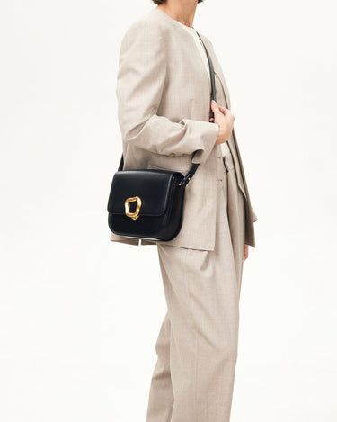 Woman wearing a beige suit carries a black calf leather Reset Tofu Bag with a gold-finish Wonton ring clasp.