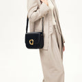 Onyx black calf leather crossbody bag with gold Wonton ring closure worn by a woman in a light beige suit.