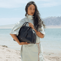 Large black Yore bowling bag made of full-grain Nappa leather with white stitching, held by a woman on a beach.