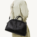 Large black Yore bowling bag made of full-grain nappa leather, worn crossbody by a person in a light green jacket.