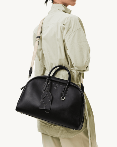 Large black Yore bowling bag made of full-grain nappa leather, worn crossbody by a person in a light green jacket.