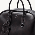 Large black Yore bowling bag made of full-grain Nappa leather with white stitching and a geometric luggage tag.