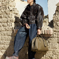 Large Yore Bowling Bag in Moss with white contrast stitching, held by a man in a leather jacket and wide-leg jeans.